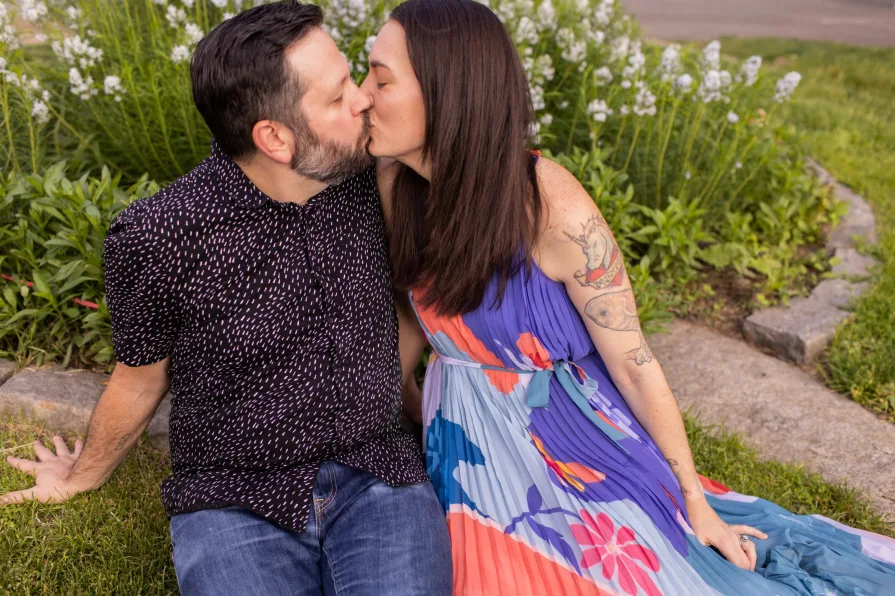 An engaged couple kissing while sitting on the grass in Schuylkill River Park.