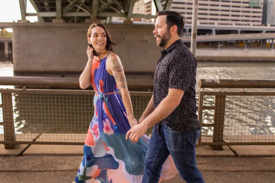 An engaged couple kissing while sitting on the grass in Schuylkill River Park.