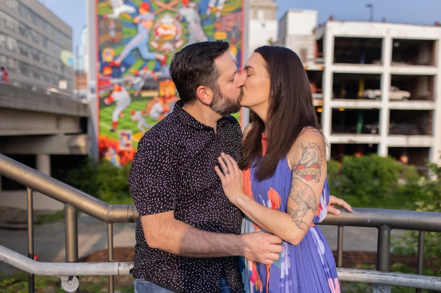 An engaged couple kissing while sitting on the grass in Schuylkill River Park.