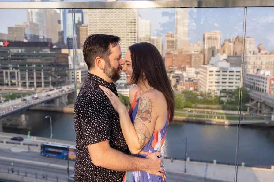 An engaged couple smiling and dancing in front of the Philadelphia skyline at Cira Green's rooftop .