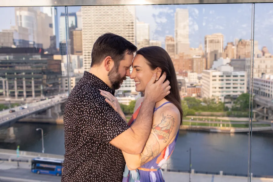 An engaged couple smiling and dancing in front of the Philadelphia skyline at Cira Green's rooftop .