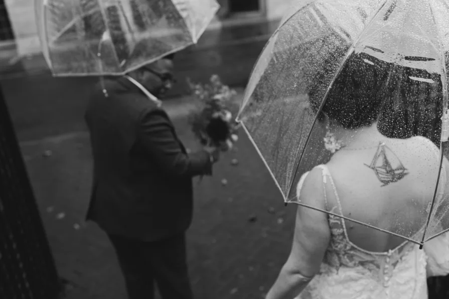 A black and white photo of a queer, biracial couple in the rain on their wedding day.
