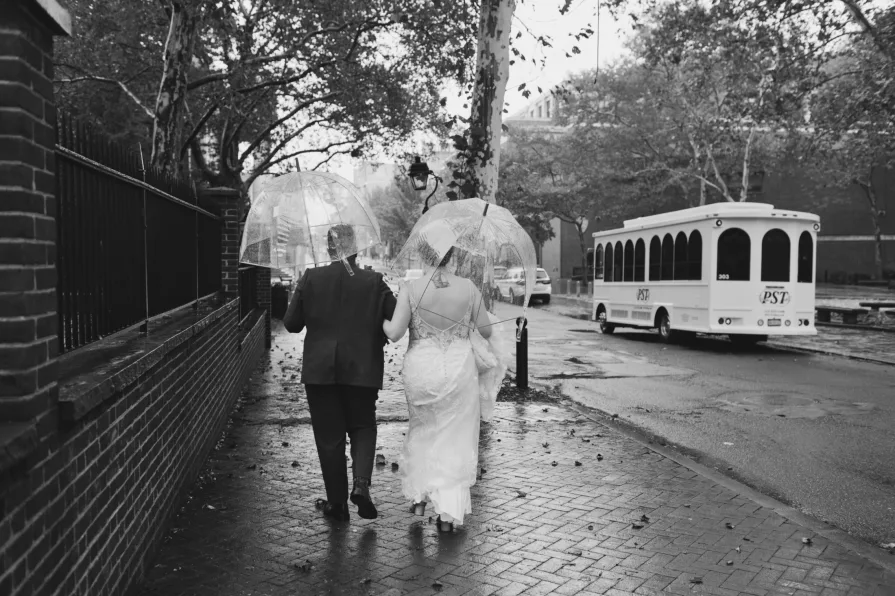 A black and white photo of a queer, biracial couple in the rain on their wedding day.
