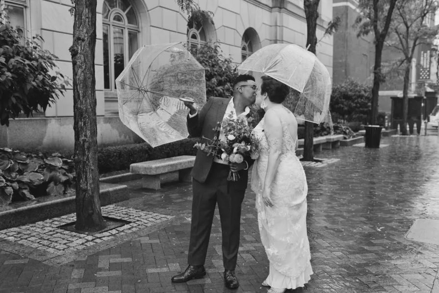 A black and white photo of a queer, biracial couple in the rain on their wedding day.