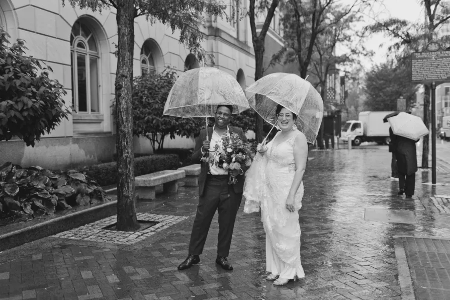 A black and white photo of a queer, biracial couple in the rain on their wedding day.