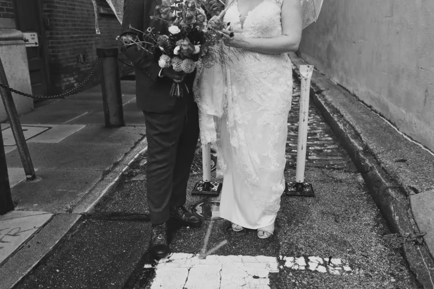 A black and white photo of a queer, biracial couple in the rain on their wedding day.