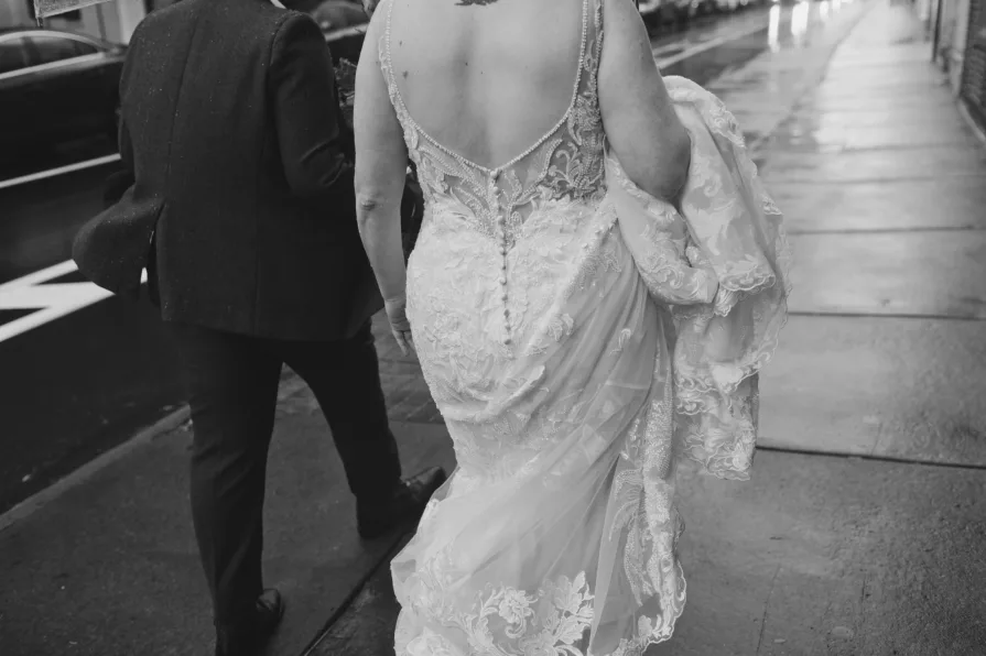 A black and white photo of a queer, biracial couple in the rain on their wedding day.