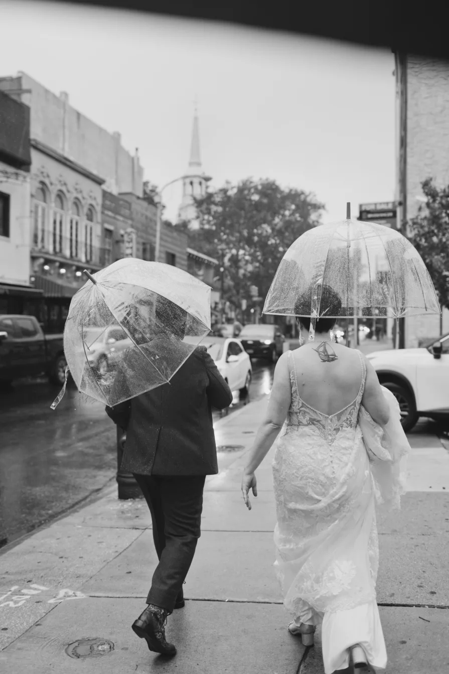 A black and white photo of a queer, biracial couple in the rain on their wedding day.