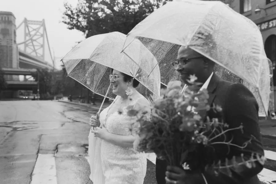 A black and white photo of a queer, biracial couple in the rain on their wedding day.