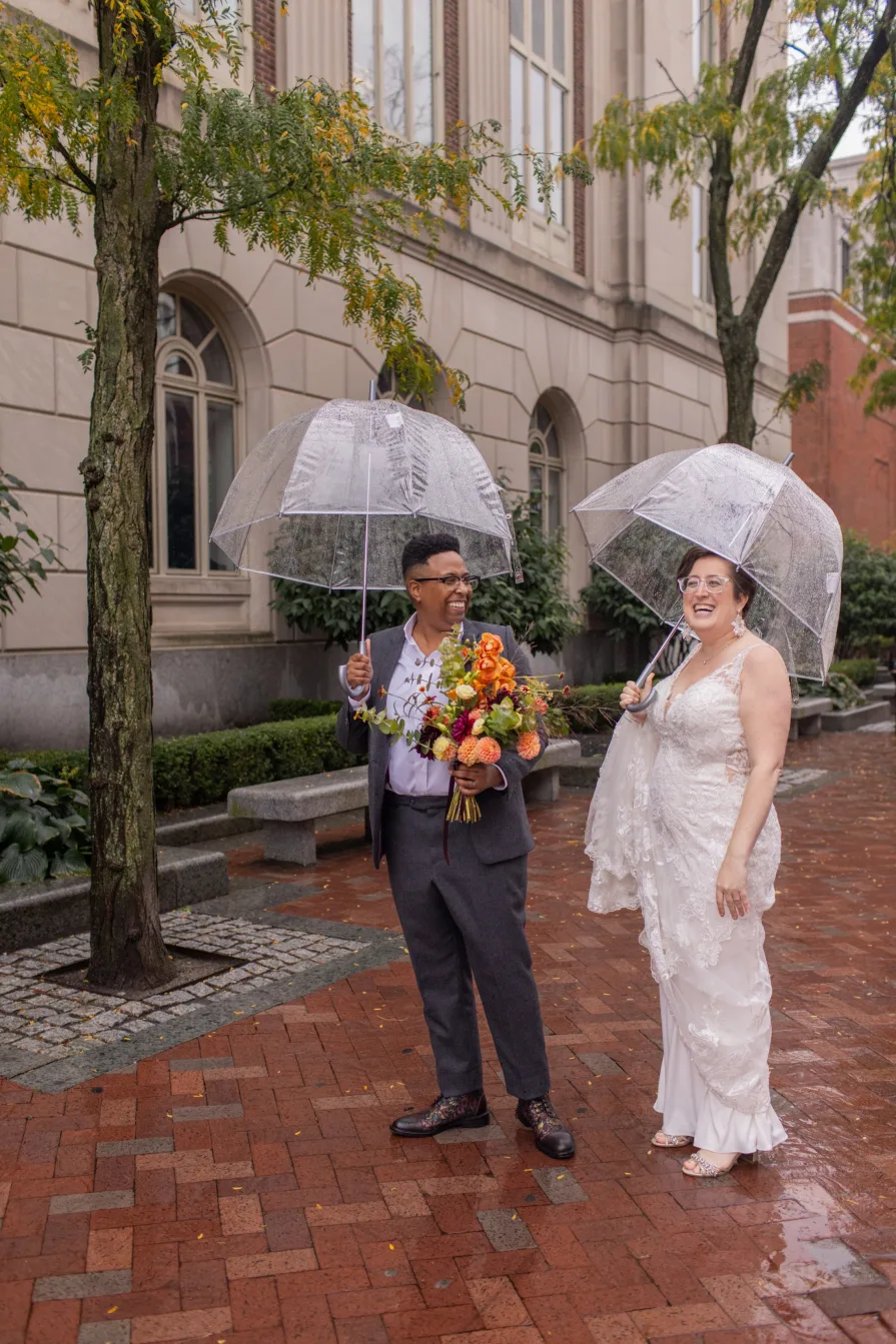 A queer, biracial couple in the rain on their wedding day.
