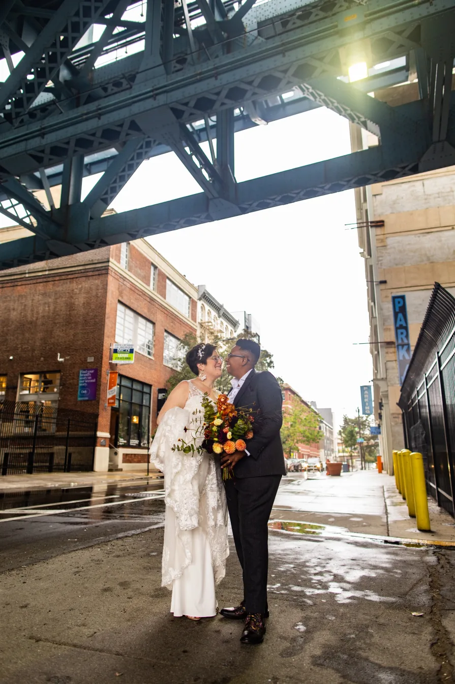 A queer, biracial couple in the rain on their wedding day under a bridge in Old City.