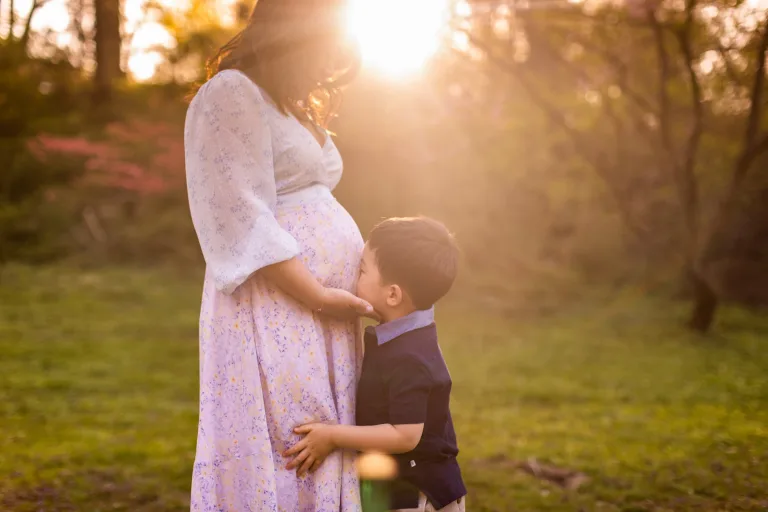 A child sweetly kissing his mom's pregnancy bump at sunset.