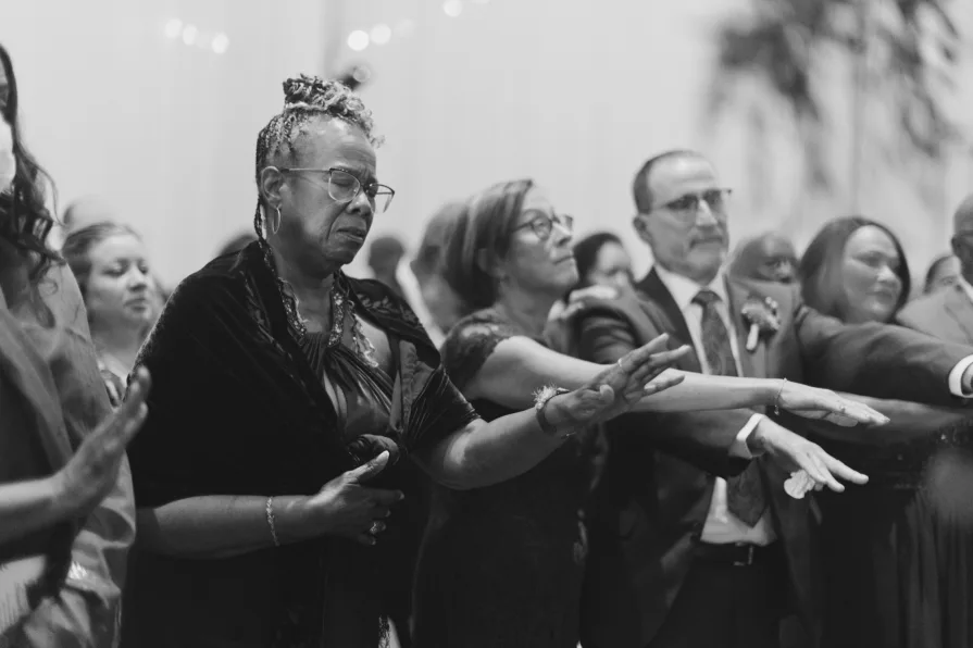 A black and white photo of guests reaching out their hands during a blessing.