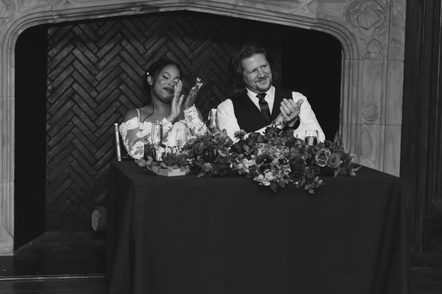 A black and white of the couple clapping during toasts.