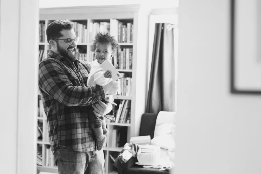 A black and white of dad with his one-year-old son in their home library.