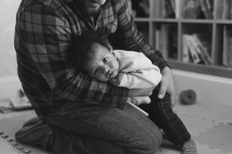 A black and white of dad with his one-year-old son in their home library.