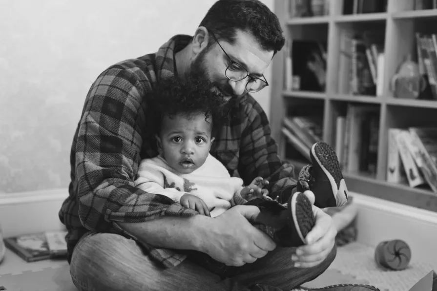 A black and white of dad with his one-year-old son in their home library.
