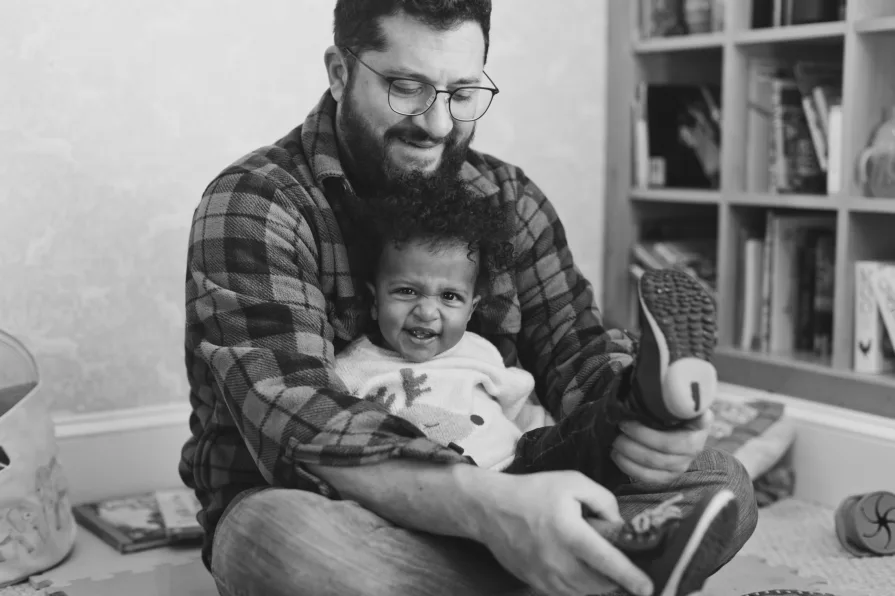 A black and white of dad with his one-year-old son in their home library.
