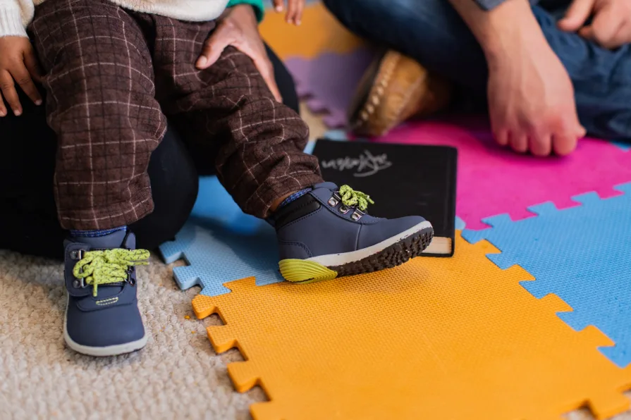 A close-up of a child's shoes on the play mat in their home.