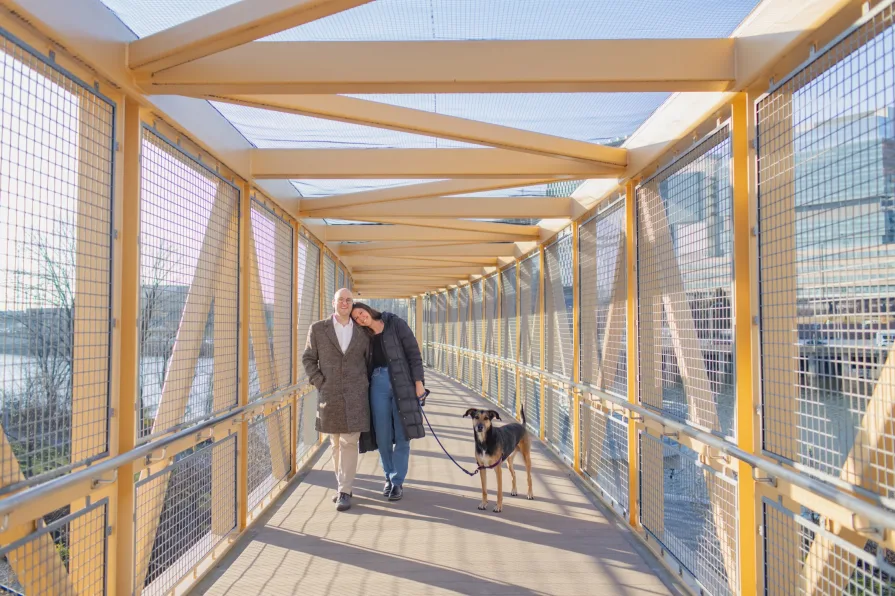 A couple smiling on a bridge after getting engaged.