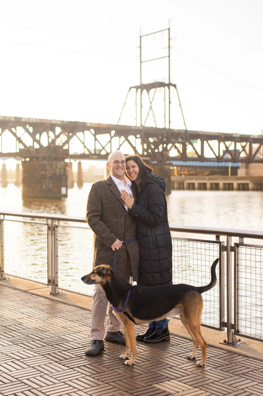 A couple walking with their dog near Schuylkill River Trail after getting engaged in Philadelphia.