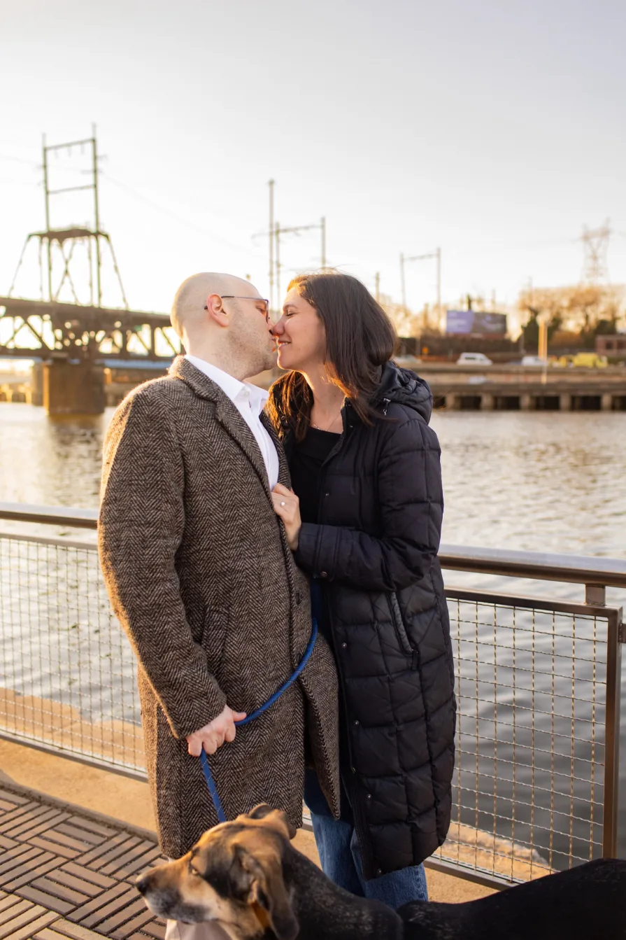 A couple walking with their dog near Schuylkill River Trail after getting engaged in Philadelphia.