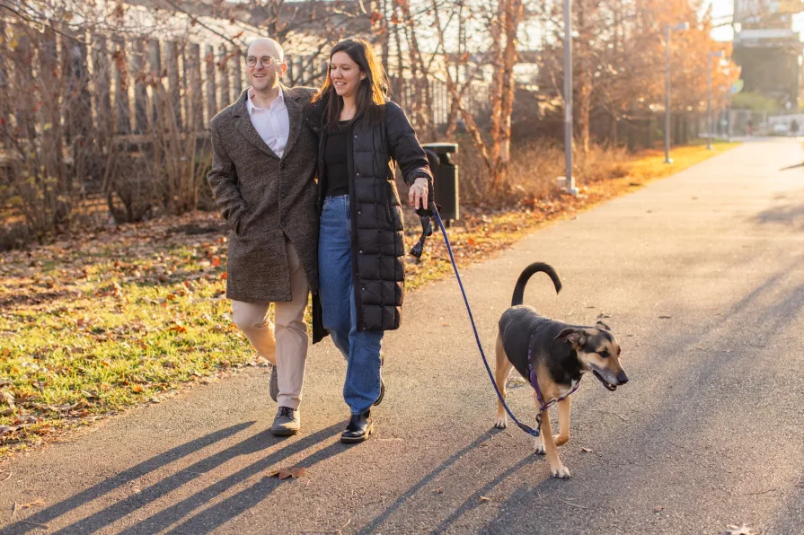 A couple walking with their dog near Schuylkill River Trail after getting engaged in Philadelphia.