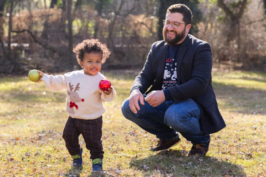 One-year-old Forest walks happily while his dad looks at him happily.