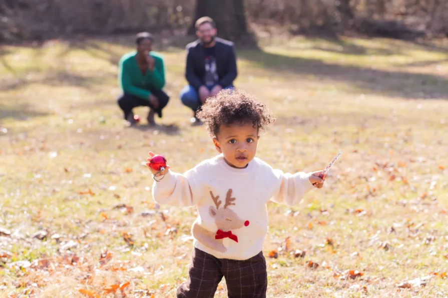One-year-old Forest walks happily while his parents look at him happily.