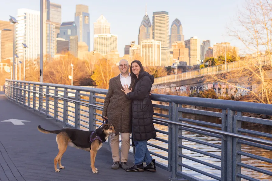 A couple walking with their dog near Schuylkill River Trail after getting engaged in Philadelphia.
