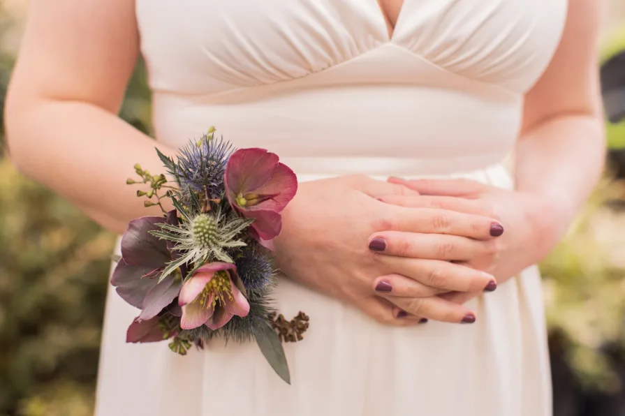 A close-up of a bride's hands interlocked while wearing a floral corsage.