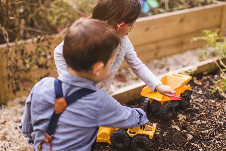 Siblings playing with trucks in their garden beds at home.